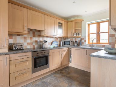A kitchen with wooden cabinets countertop microwave toaster oven and window at Lundy Cottage in Rock