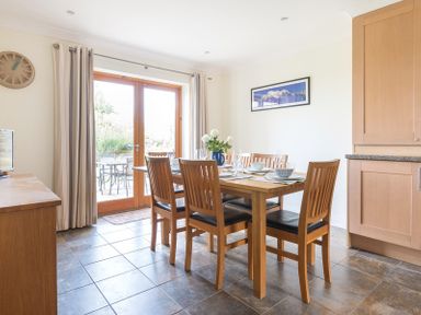 A dining room with a wooden table and six chairs set with dishes and glasses next to glass doors at Lundy Cottage in Rock