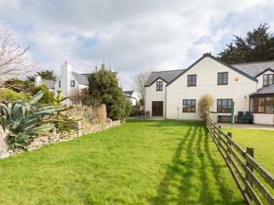 A grassy backyard with a wooden fence and patio furniture next to a white house at Lundy Cottage in Rock