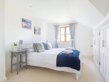A bedroom with a white bed with pillows and towels by a window with curtains at Lundy Cottage in Rock