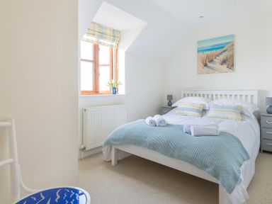 A bedroom with a double bed blue blanket and window with striped curtain at Lundy Cottage in Rock