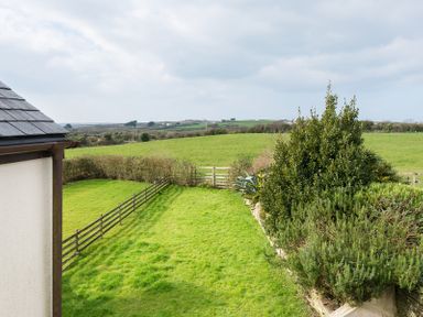 A fenced garden with green grass and bushes overlooking open fields at Lundy Cottage in Rock