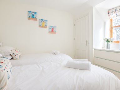 A bedroom with two beds with white bedding a window with a floral curtain and a dresser with flowers at Lundy Cottage in Rock