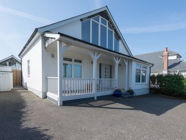 A white house with a porch and large triangular window at The Point in Polzeath