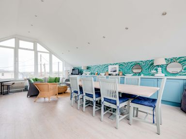 A dining area with a long table and chairs and a seating area with sofas and green cushions at The Point in Polzeath