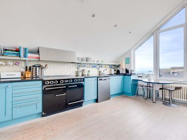 A kitchen with blue cabinets a black oven dishwasher and a table by large windows at The Point in Polzeath
