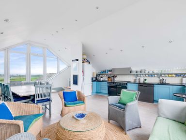 An open living room and kitchen area with wicker chairs and blue cushions at The Point in Polzeath