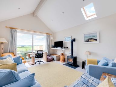 A living room with sofas a desk a wood stove and large window with outdoor seating at The Point in Polzeath