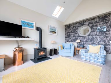 A living room with a wood stove two armchairs a yellow rug and a wall mirror at The Point in Polzeath