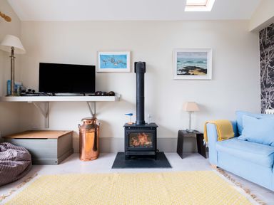 A living room with a wood stove television blue sofa and yellow rug at The Point in Polzeath