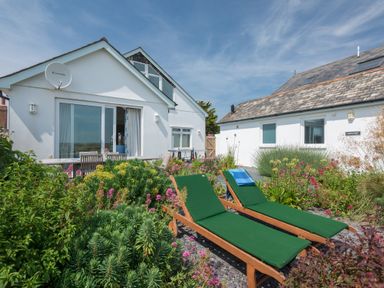 An outdoor garden area with two green lounge chairs and a dining table in front of white houses at The Point in Polzeath