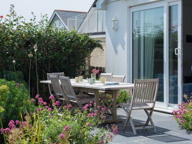 An outdoor patio with a wooden dining table and chairs surrounded by plants and flowers at The Point in Polzeath