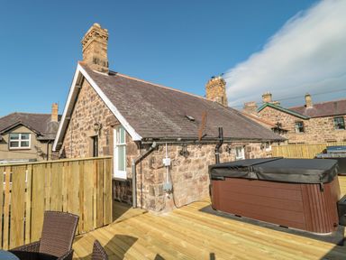 An outdoor deck area with a hot tub wooden fencing and stone houses in the background at Cheviot Hills in Wooler