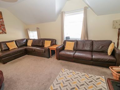 A living room with two dark brown leather sofas with yellow cushions a wooden side table beige curtains and a patterned rug at Cheviot Hills in Wooler