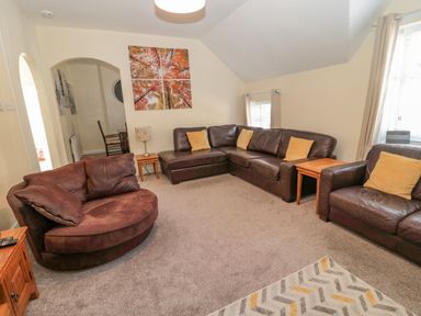 A living room with brown leather sofas yellow cushions side tables lamp and a wall painting at Cheviot Hills in Wooler