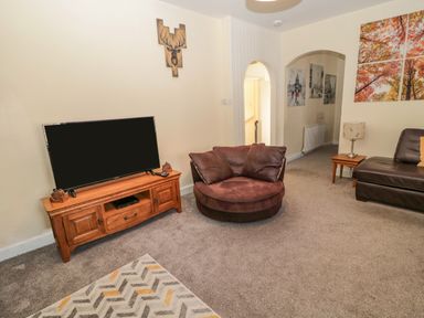 A living room with a television on a wooden stand a round brown chair a brown leather sofa and wall art at Cheviot Hills in Wooler