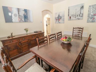 A dining room with a dark wooden table and chairs and a sideboard with a bowl of fruit and wall art at Cheviot Hills in Wooler