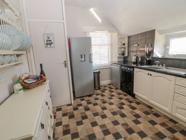 A kitchen with checkered floor tiles a silver refrigerator a white cupboard with dishes and food items and black countertop at Cheviot Hills in Wooler