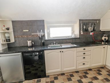 A kitchen with white cabinets black countertops a sink a dishwasher a small refrigerator knives hanging utensils on a wall rack and a kettle at Cheviot Hills in Wooler