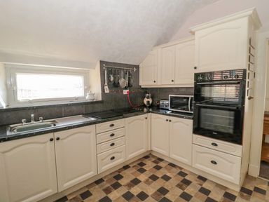 A kitchen with white cabinets black countertops a sink a microwave toaster coffee machine oven and kitchen utensils hanging at Cheviot Hills in Wooler