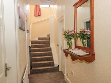 A hallway with carpeted stairs a wall mirror a wooden shelf with flowers and a book at Cheviot Hills in Wooler