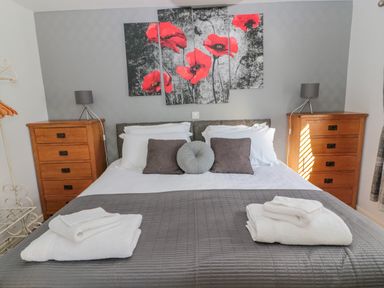 A bedroom with a double bed two wooden dressers bedside lamps and red flower wall art at Cheviot Hills in Wooler