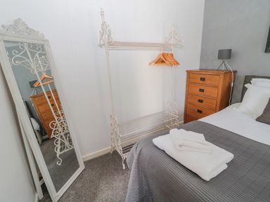 A bedroom with a bed covered with gray bedding and white towels on it a wooden chest of drawers a standing mirror and a white metal clothes rack with wooden hangers at Cheviot Hills in Wooler
