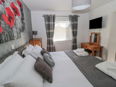 A bedroom with a double bed white bedding grey pillows a wooden desk with a mirror a wall-mounted TV and grey striped curtains at Cheviot Hills in Wooler