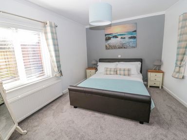 A bedroom with a double bed two bedside tables with lamps a window with checkered curtains and a wall painting at Cheviot Hills in Wooler