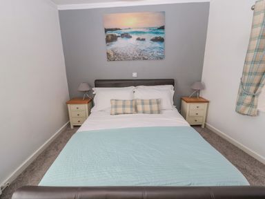 A bedroom with a bed two bedside tables with lamps and a seascape picture on the wall at Cheviot Hills in Wooler