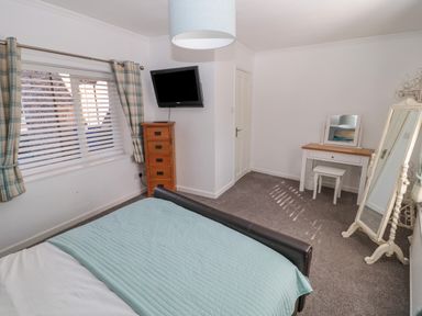 A bedroom with a bed a television on a wooden chest of drawers a dressing table with a stool and a full length mirror at Cheviot Hills in Wooler