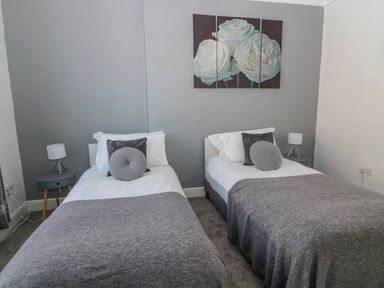 A bedroom with two single beds side by side each with grey and white bedding and round pillows and a bedside table with a lamp at Cheviot Hills in Wooler
