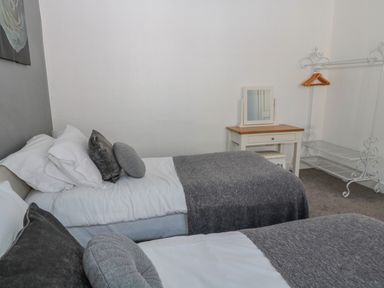 A bedroom with two single beds with grey blankets a white desk with a mirror and a white clothing rack with hangers at Cheviot Hills in Wooler