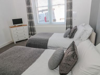 A bedroom with two single beds with pillows and grey blankets a white chest of drawers with a small television and a window with curtains at Cheviot Hills in Wooler