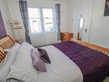 A bedroom with a wooden bed a chest of drawers and a window with curtains at Cheviot Hills in Wooler