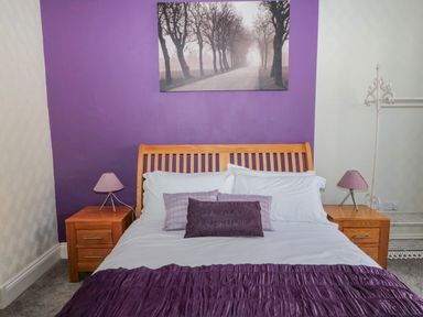 A bedroom with a wooden bed and purple decorated wall at Cheviot Hills in Wooler