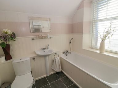 A bathroom with a bathtub a sink toilet a flower vase and a window with blinds at Cheviot Hills in Wooler