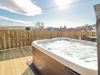 An outdoor wooden deck with a hot tub and a table with chairs at Cheviot Hills in Wooler