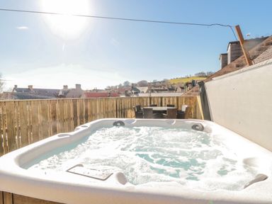 An outdoor hot tub with bubbling water and a round table with chairs behind a wooden fence at Cheviot Hills in Wooler