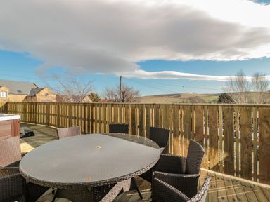 An outdoor patio with a round glass table and six wicker chairs surrounded by a wooden fence at Cheviot Hills in Wooler