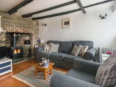 A living room with a stone fireplace grey couches wooden coffee table and striped rug at Cloam Cottage in Port Isaac