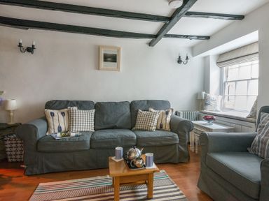 A living room with a grey sofa and armchair a small wooden coffee table and window seat at Cloam Cottage in Port Isaac