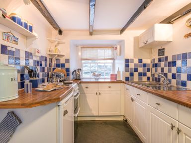 A kitchen with white cabinets wooden countertops blue and white tiled walls and a window at Cloam Cottage Port Isaac