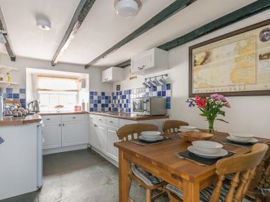 A kitchen with white cabinets a wooden table set with dishes and flowers on the table at Cloam Cottage in Port Isaac