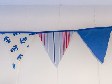 A row of triangular fabric bunting with blue anchors stripes and solid blue hanging on a white tiled wall at Cloam Cottage in Port Isaac