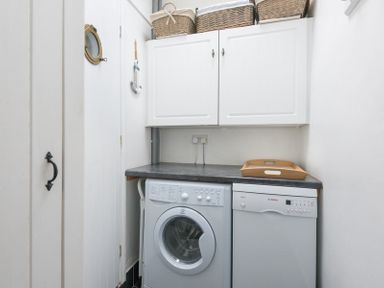 A utility room with a washing machine dishwasher countertop white cabinets and wicker baskets at Cloam Cottage Port Isaac