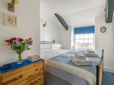 A bedroom with a bed and folded towels on top and a dresser with flowers at Cloam Cottage in Port Isaac