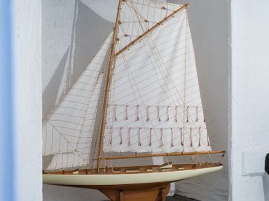 A scale model of a sailboat with white sails in a white walled room at Cloam Cottage in Port Isaac