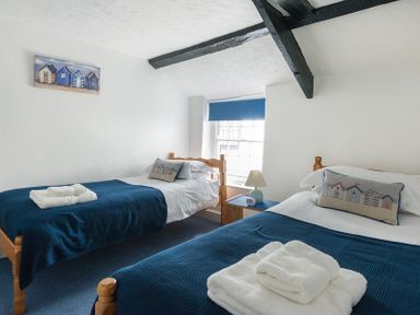 A bedroom with two single beds blue blankets white walls a window with blue blind and a small lamp on a wooden table at Cloam Cottage in Port Isaac