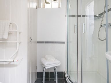 A bathroom with a glass shower enclosure a stool with folded towels and a wall-mounted towel rack at Cloam Cottage in Port Isaac